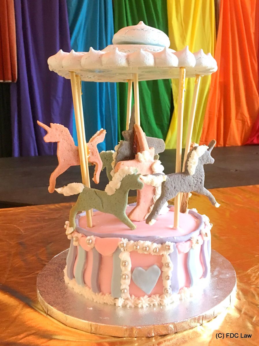 pink, lavender and grey cake in the shape of a fairground carousel, against a rainbow flag backdrop