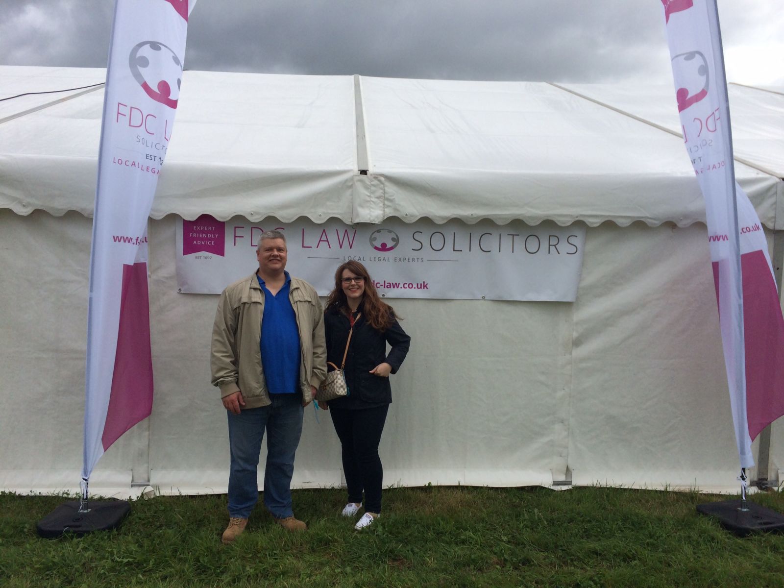 man and woman standing in front of marquee, between 2 feather flags showing the FDC law logo