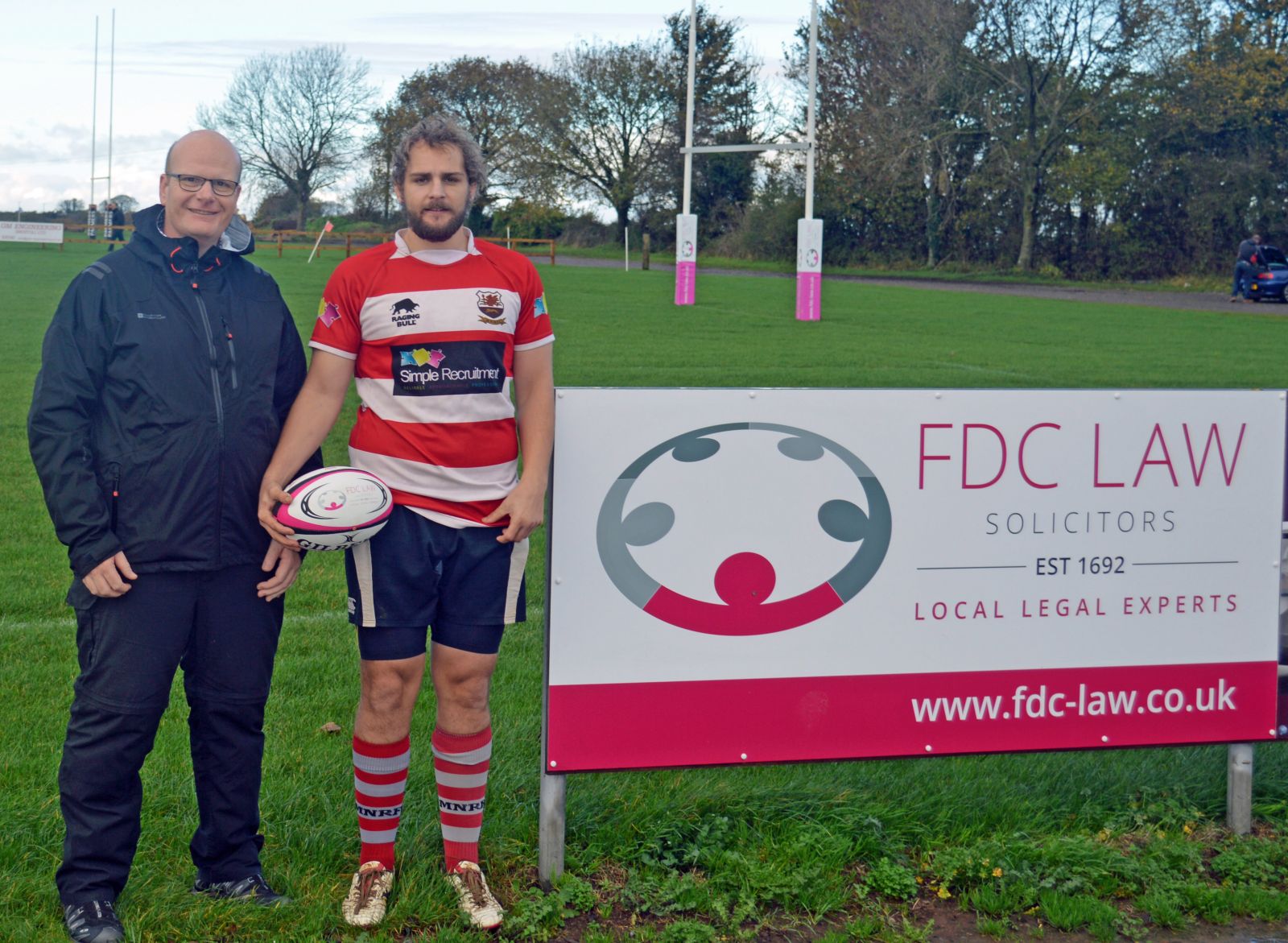 two men with FDC Law rugby ball standing by advertising board