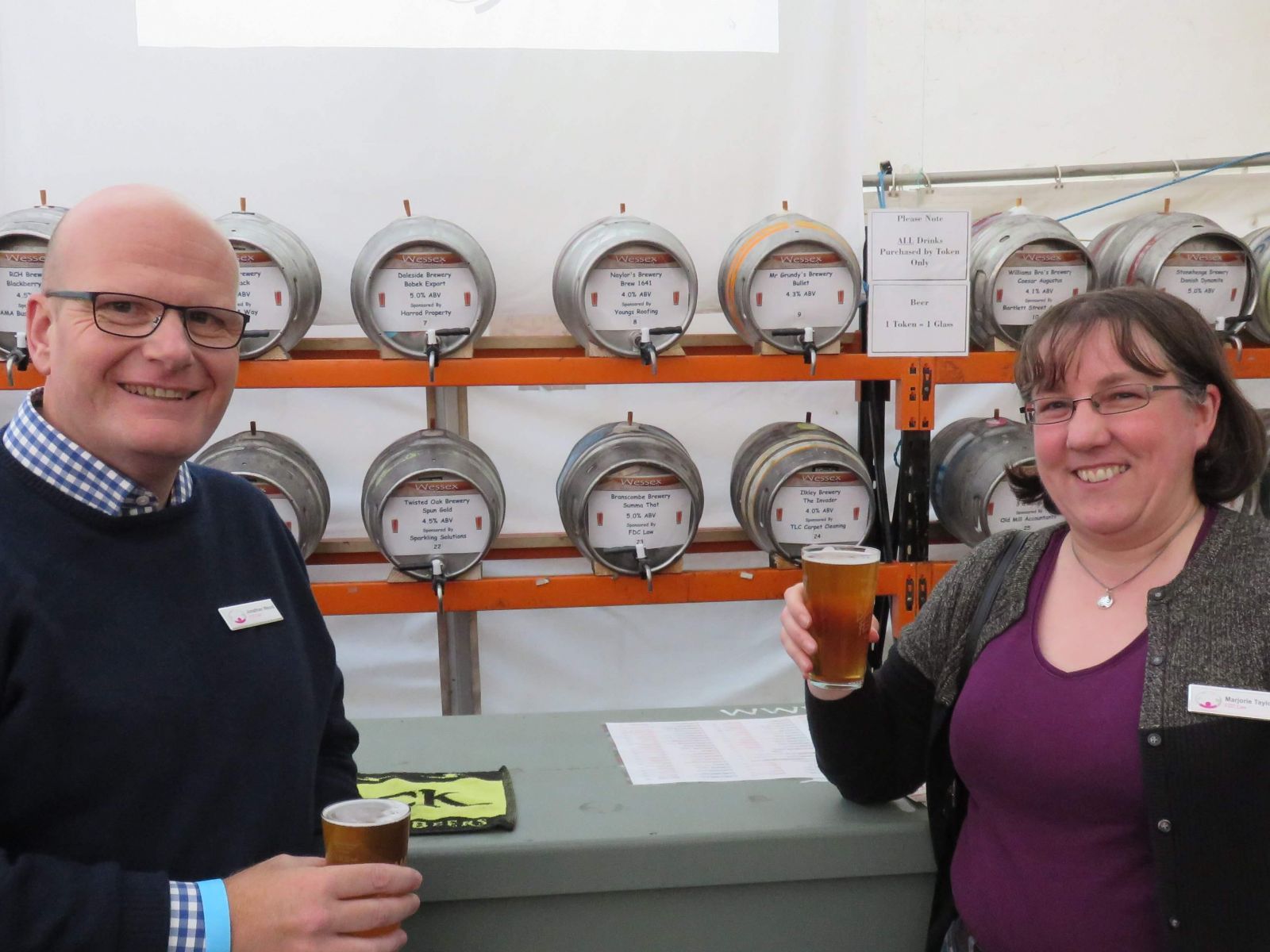 Photo shows a man,Jonathan Wood and woman  Marjorie Taylor standing in front  of rows of beer kegs, holding drinks